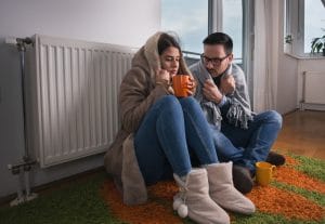 heater repair service - Couple sitting beside radiator 300x207 -