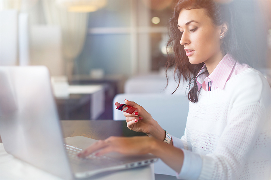 Woman looking at the back of her red credit card before making a purchase online