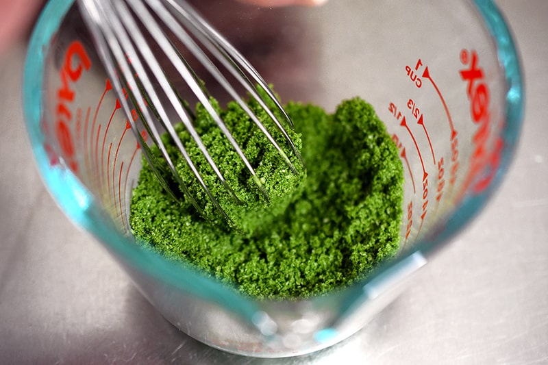 An overhead shot of a whisk combining the dry ingredients of paleo matcha mug cake in a measuring cup.