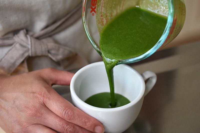 Someone pouring paleo matcha mug cake batter from a liquid measuring cup into a white coffee mug.